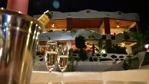A table with a champagne flute and a glass, set against a building with outdoor lighting and plants. - Mirabel Resort & Mini Golf (Pattaya)
