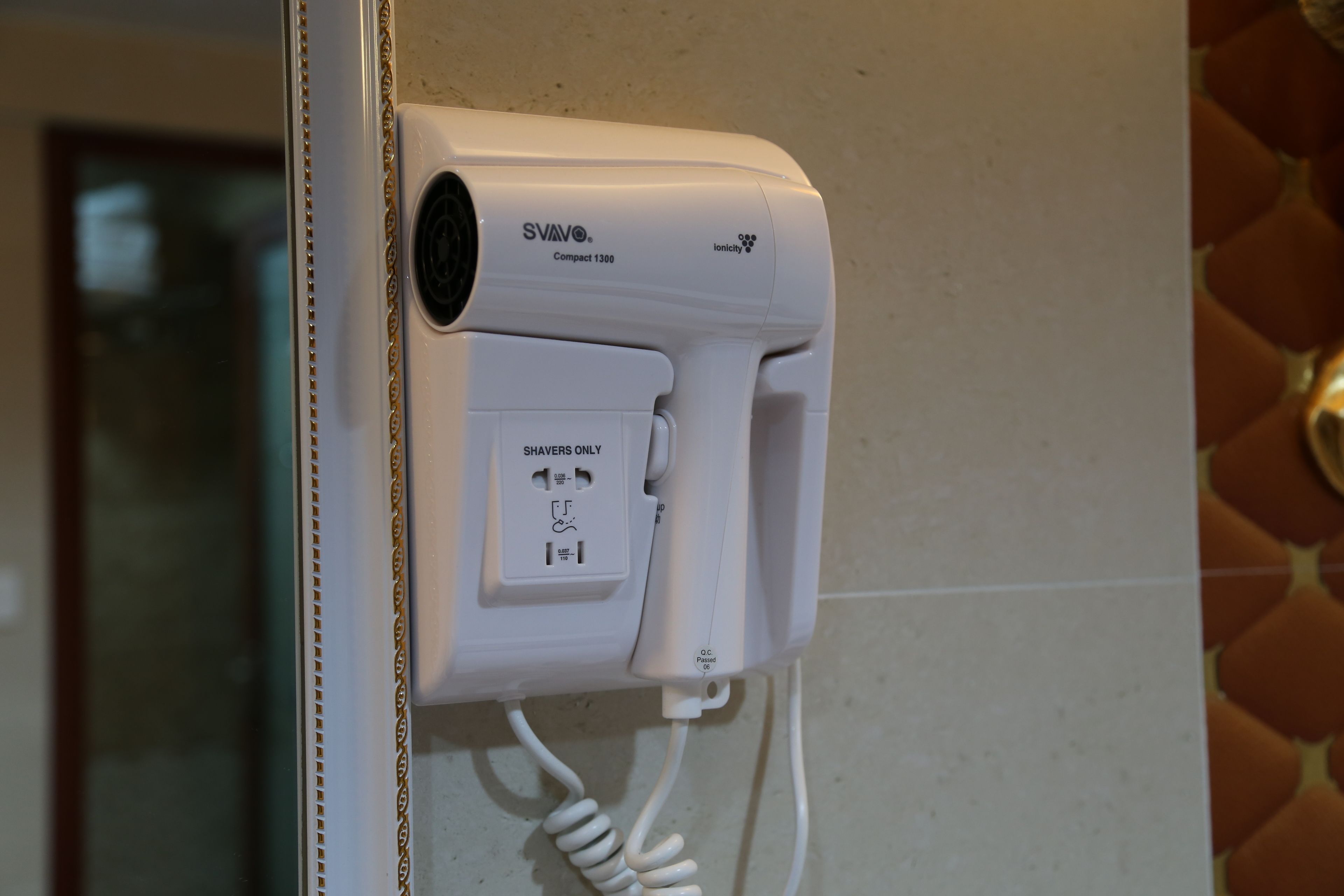 Un secador de pelo SVAVO Compact 1300 blanco montado en la pared con un cable enrollado.