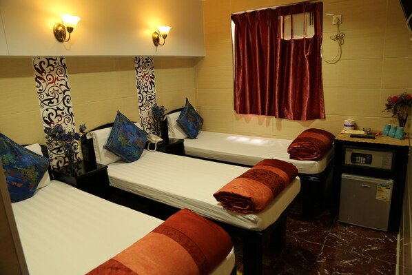 Habitación de hotel con tres camas, cada una con almohadas estampadas, un refrigerador pequeño y una mesita de noche con control remoto.