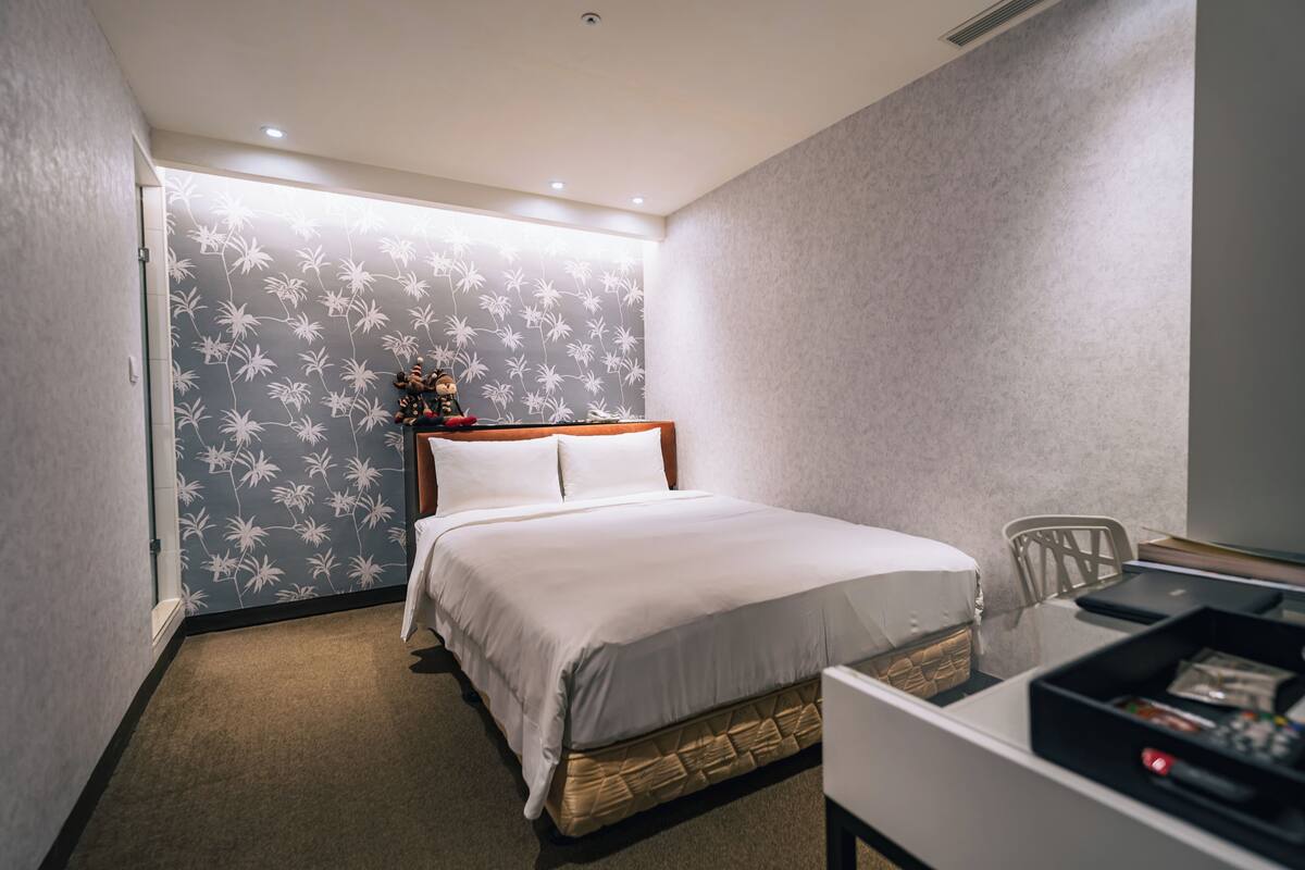 Habitación de hotel con cama, escritorio y silla, y pared con diseño floral.