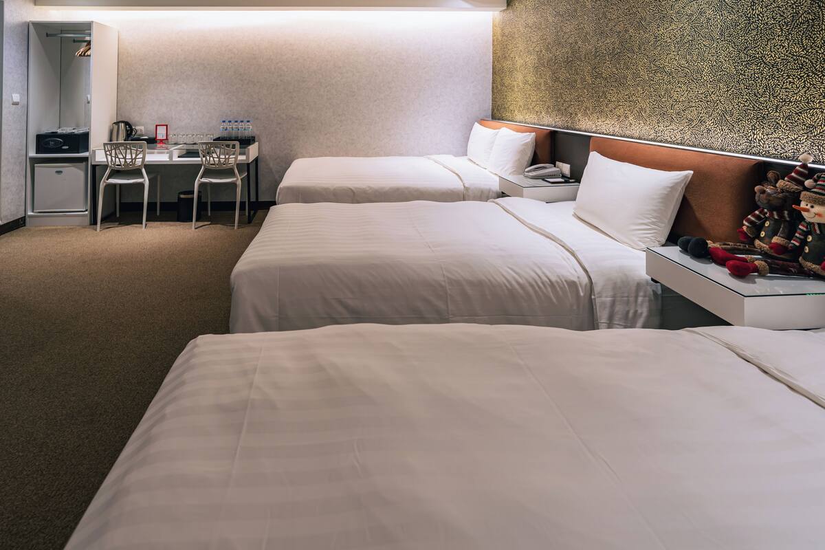 Habitación de hotel con dos camas, un escritorio con sillas, un minibar y un adorno en la pared.
