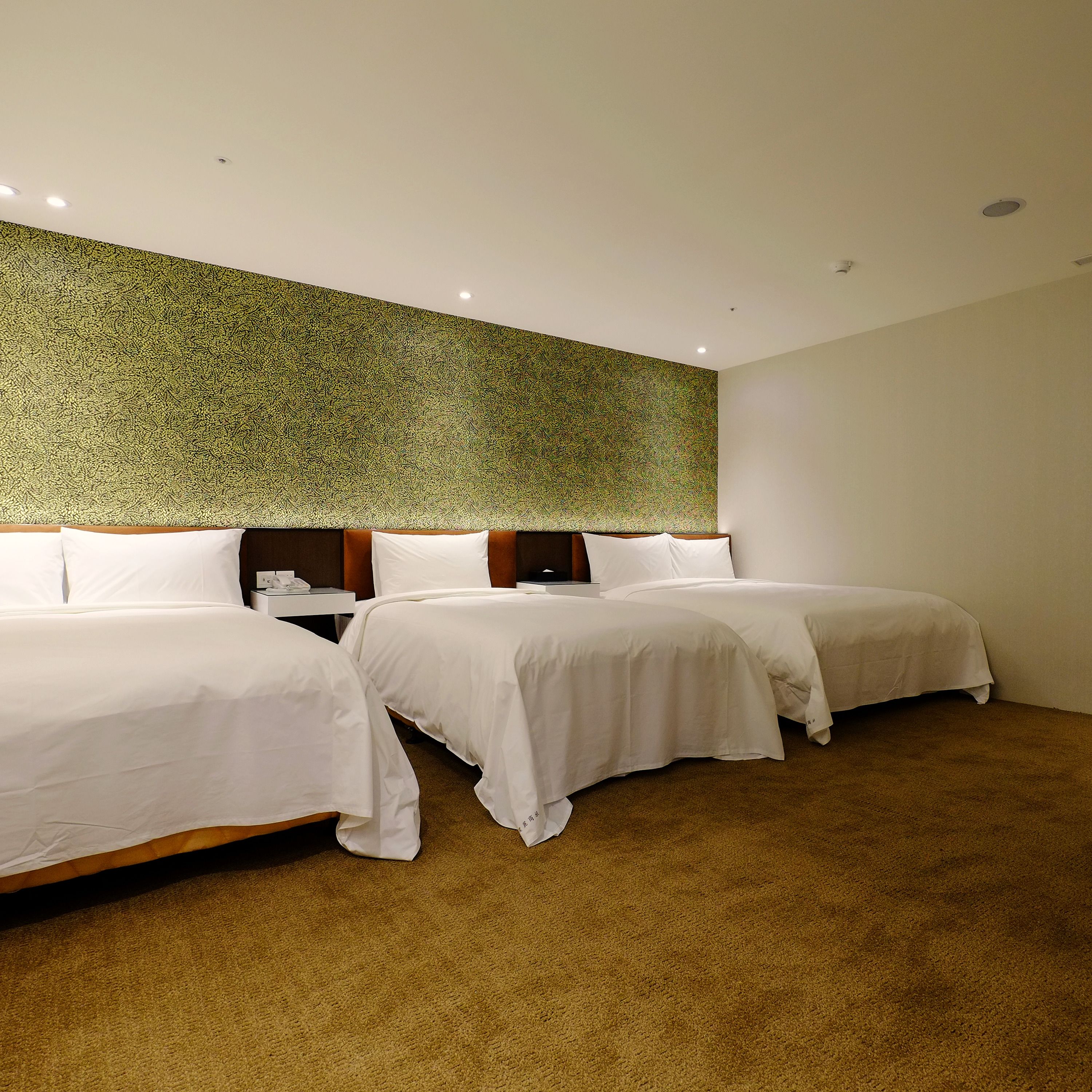 A hotel room with two beds, a patterned wall, and a carpeted floor.