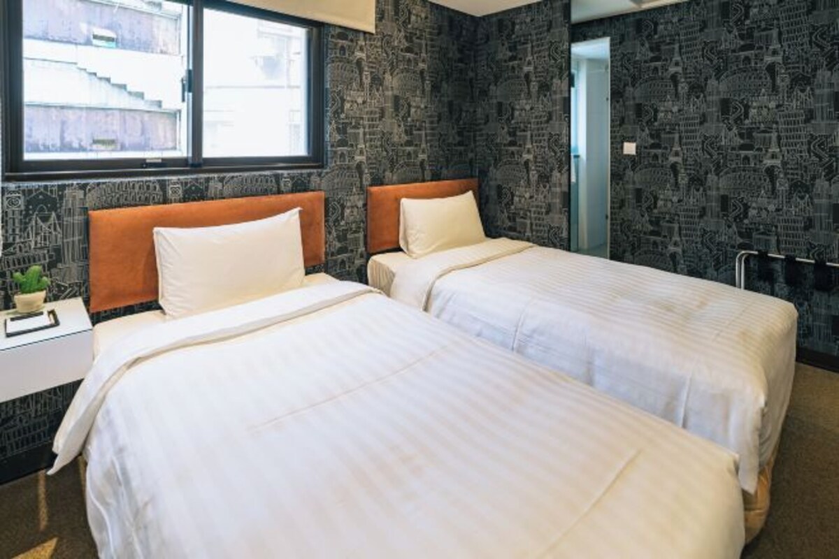 A hotel room with two beds, a nightstand, and a window.
