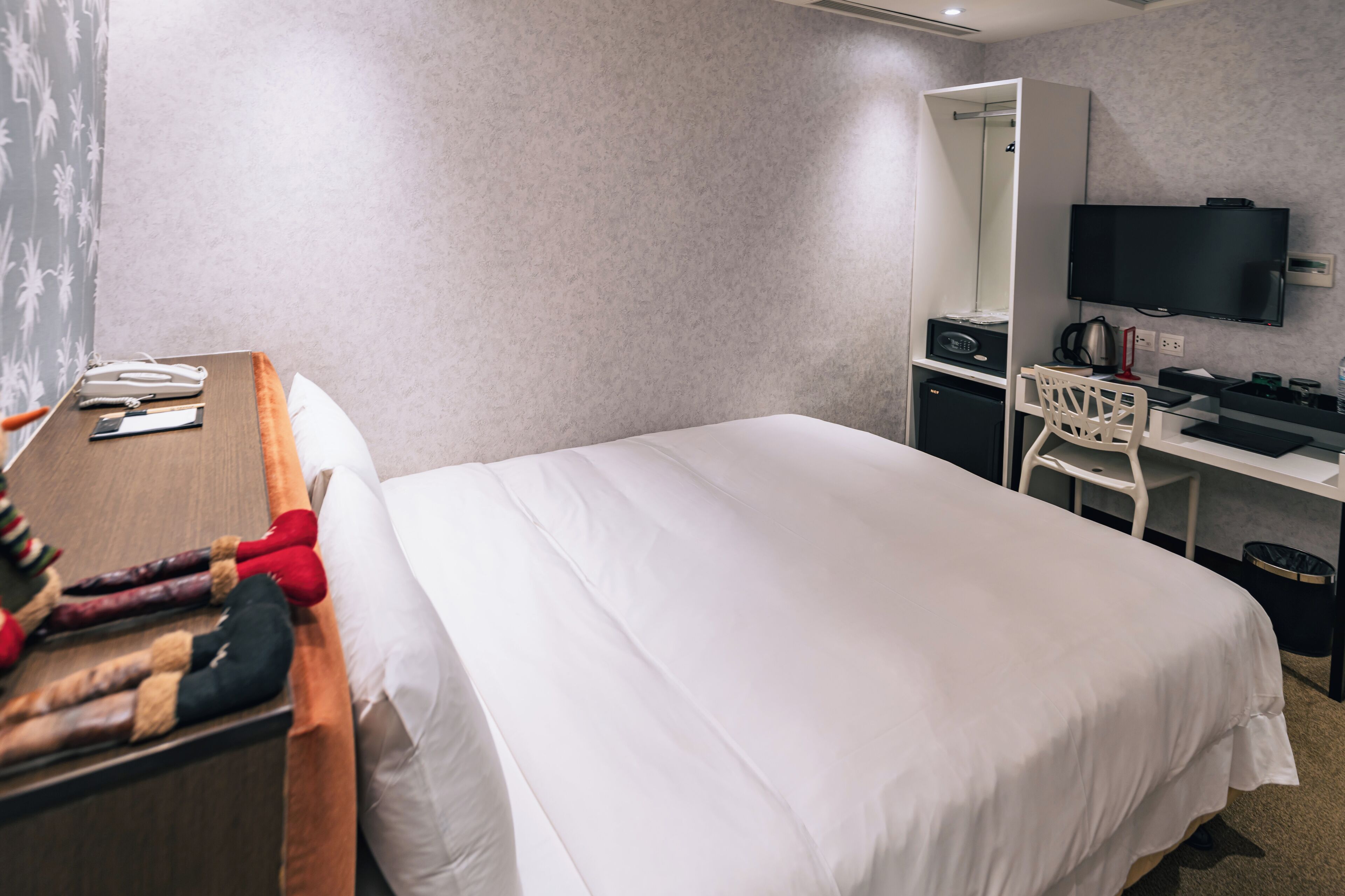 Una habitación de hotel con cama, escritorio, silla, televisor y armario.