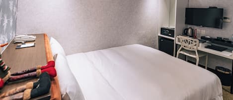 Una habitación de hotel con cama, escritorio, silla, televisor y armario.