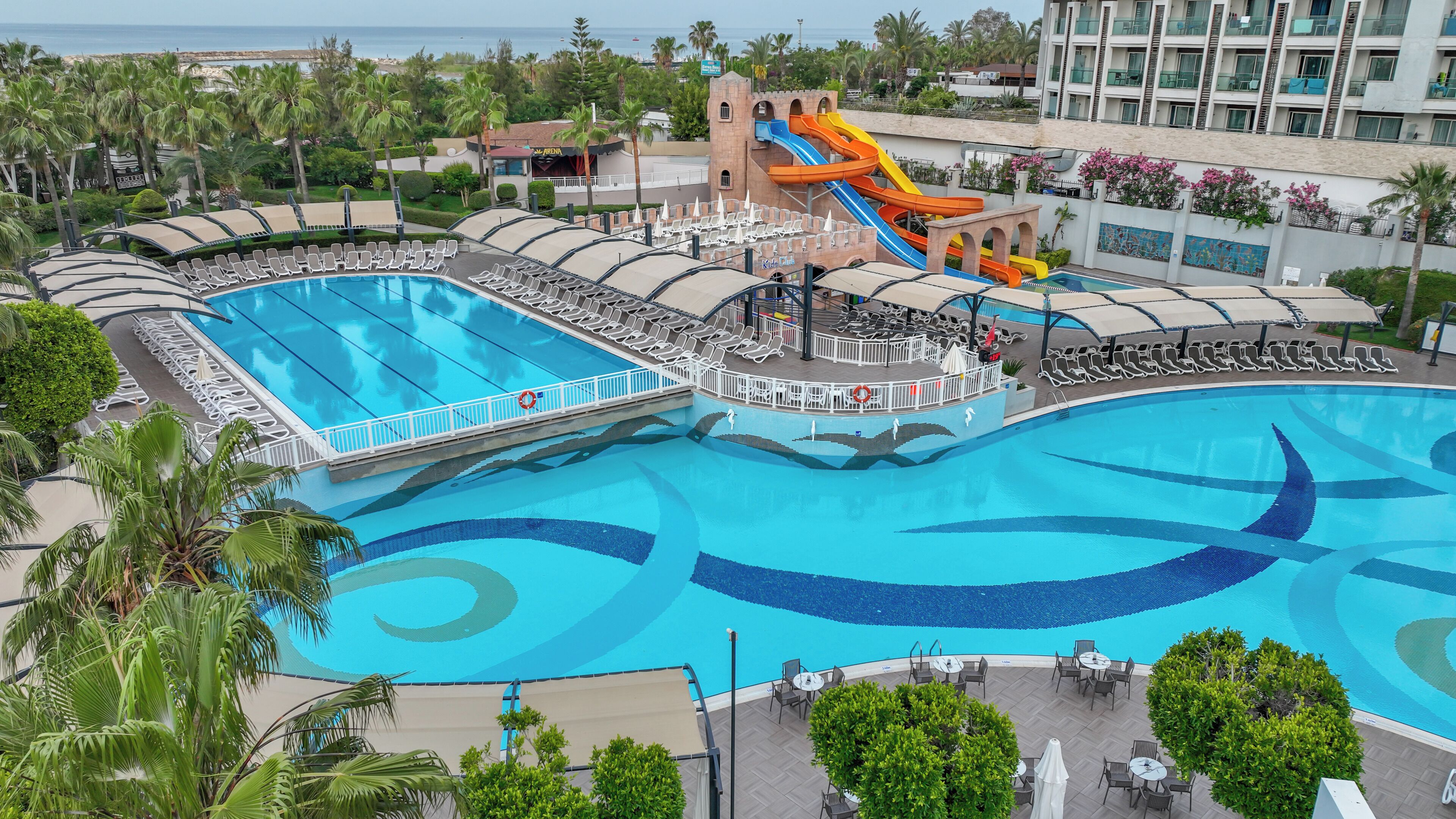 A large swimming pool with a water slide, lounge chairs, and a view of the ocean.