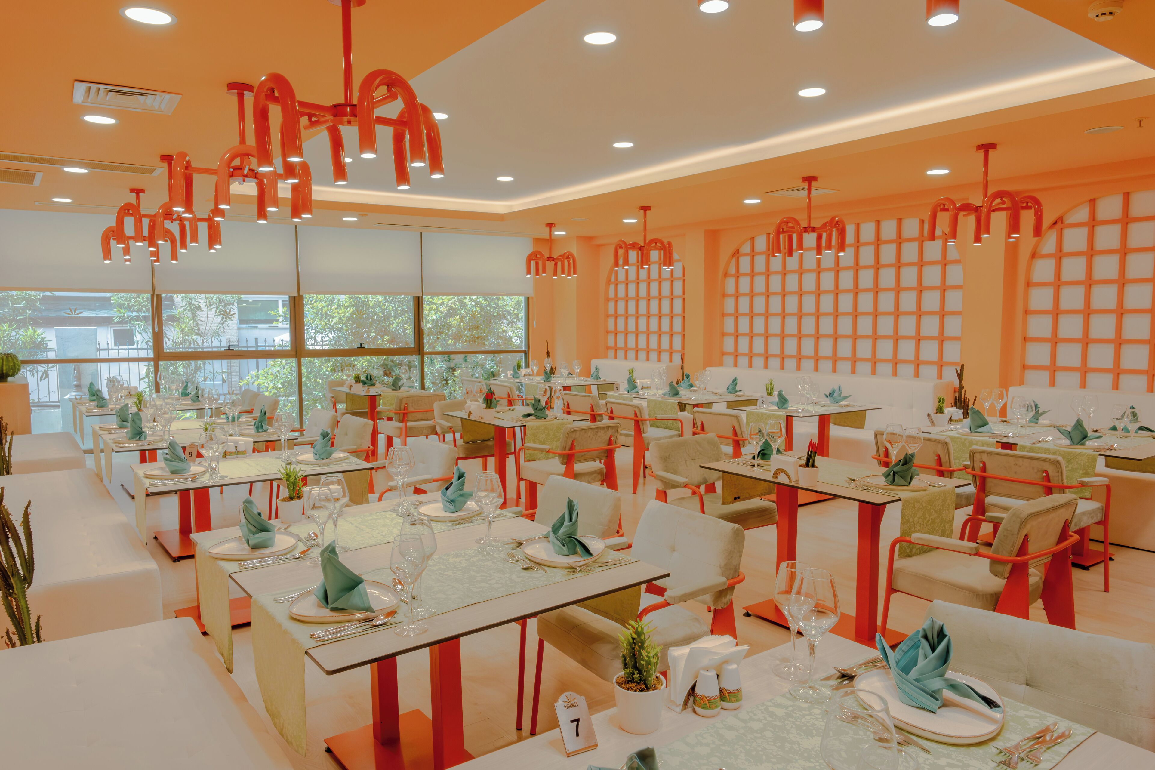 Un restaurante con mesas dispuestas para comer, con un diseño moderno y detalles en naranja, y amplias ventanas.