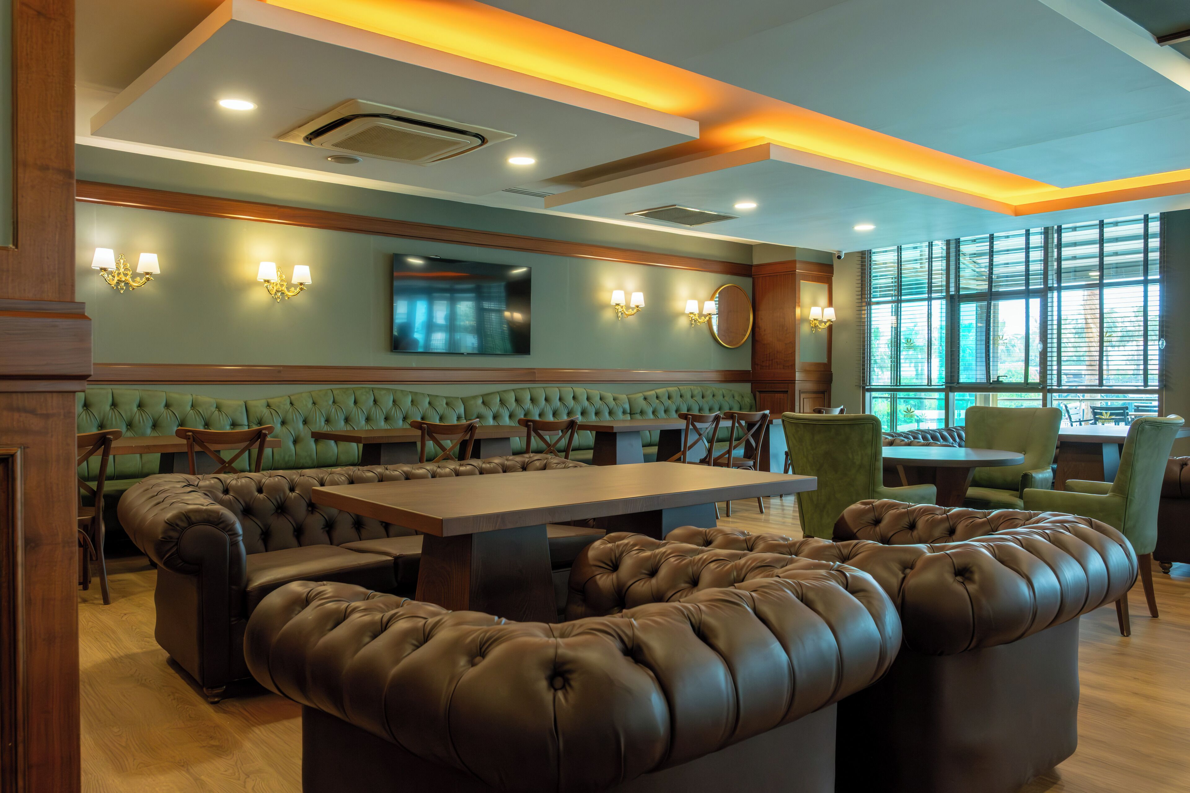 A restaurant with green upholstered booths, a large wooden table, and wall-mounted lighting.