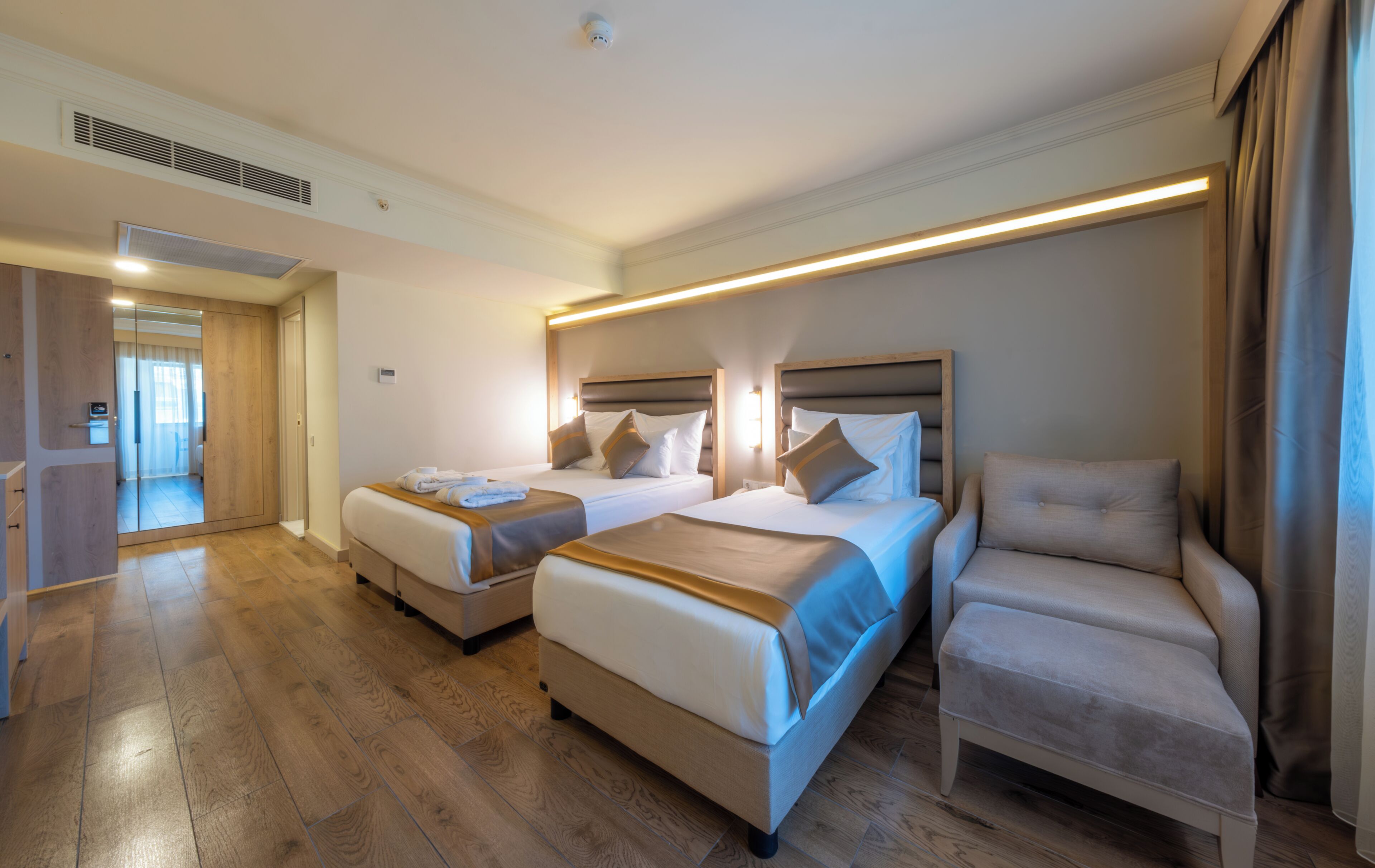 A hotel room with two beds, a chair, and a mirror.