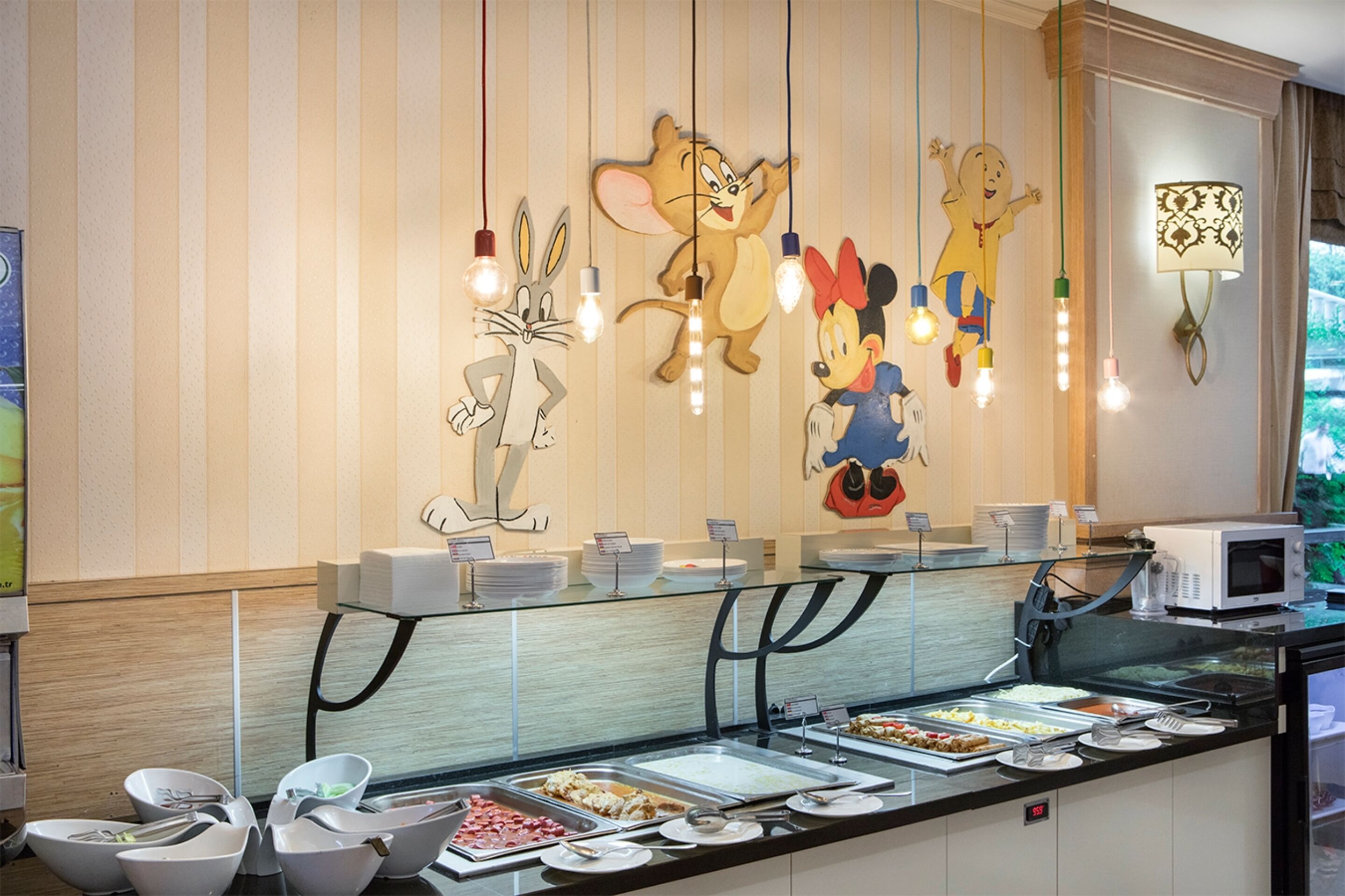 A buffet area with various food stations, a microwave, and a wall decorated with cartoon characters.