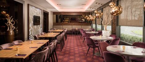 A restaurant with hexagonal patterned flooring, multiple dining tables with chairs, and pendant lighting.