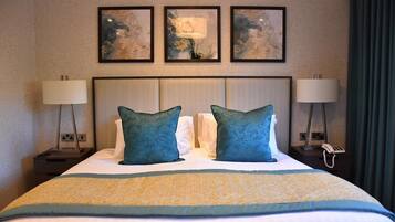 A hotel room with a large bed, two pillows, a bedside table with a lamp, a phone, and three framed artworks on the wall.
