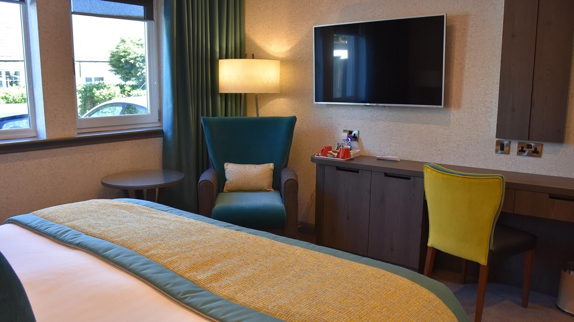 A hotel room with a bed, a desk, a chair, a TV, and a window with curtains.