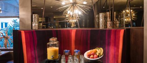 A dining area with a booth, a fruit bowl, a juice dispenser, and a decorative light fixture.