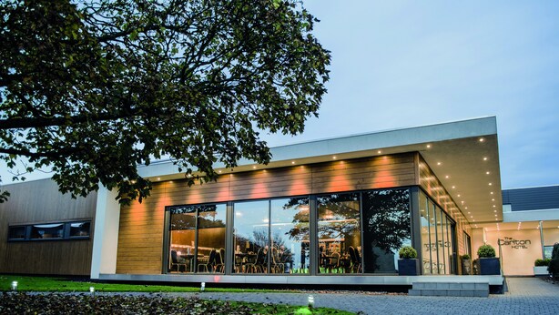 A modern hotel with large glass windows, a wooden facade, and a well-lit entrance.