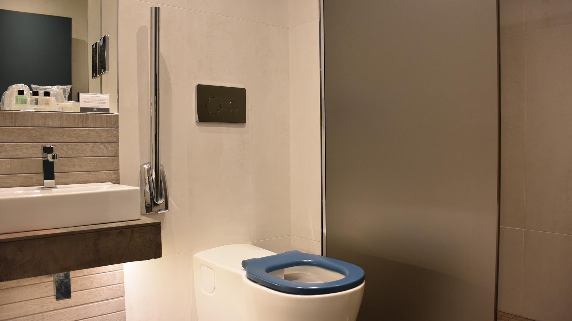 Une salle de bain moderne avec un lavabo blanc, des toilettes bleues et une douche à parois de verre.