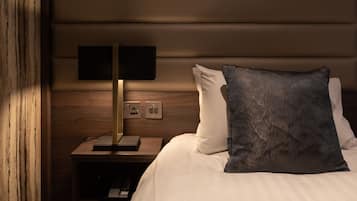 A neatly made bed with white linens and a dark patterned pillow, a bedside table with a lamp, and a wooden headboard.