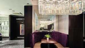 A modern hotel lobby with a reception desk, a seating area with a table and chairs, and a decorative chandelier.