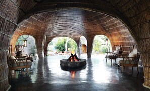 Um espaço circular com uma lareira no centro, rodeado por mobiliário de madeira e arcos.