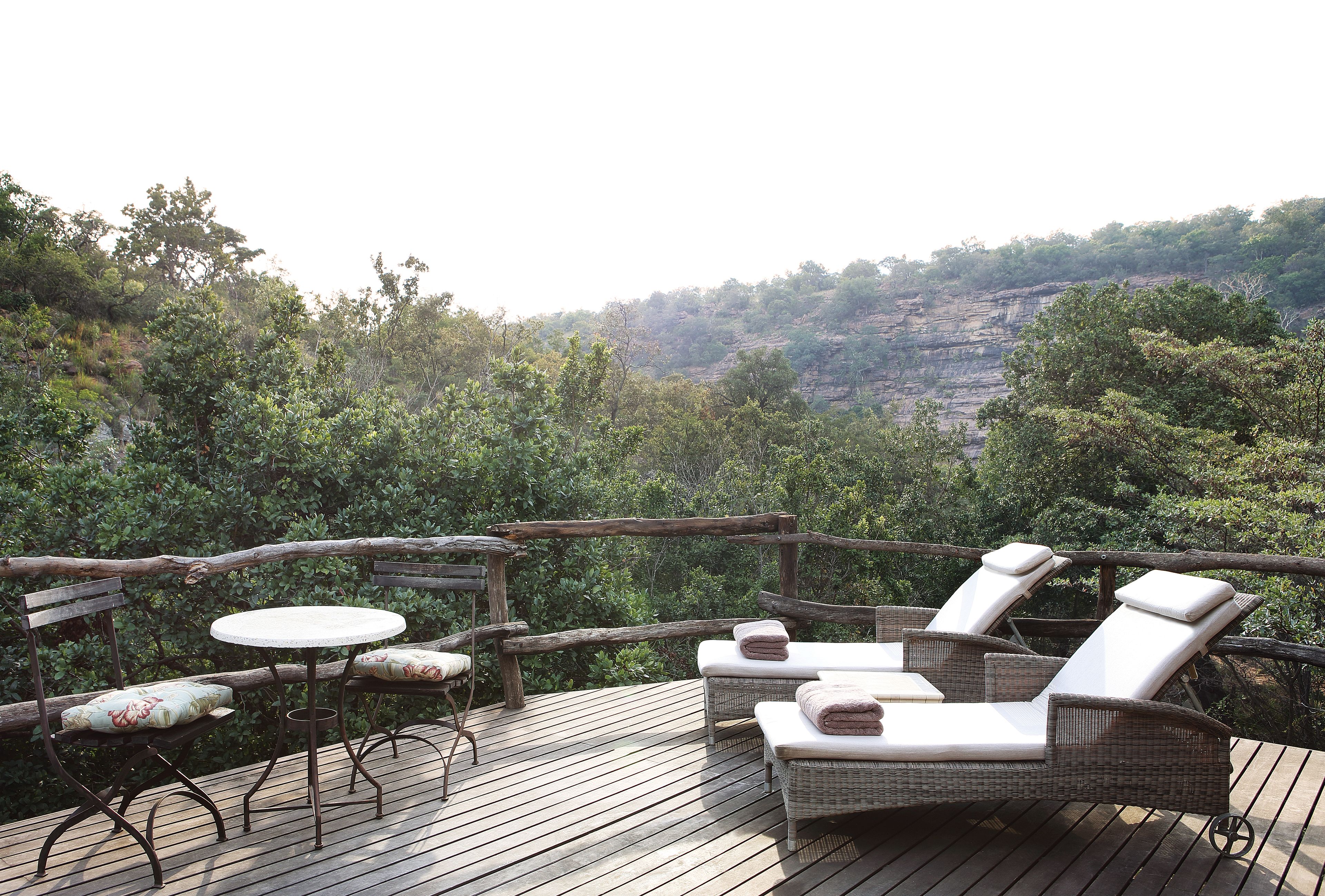 A wooden deck with wicker lounge chairs and a table, overlooking a lush forested area.