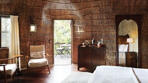 Een kamer met een houten plafond, een bed, een stoel, een tafel en uitzicht op het omliggende landschap.