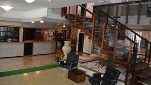 A spacious lobby with a wooden floor, a seating area with chairs, a large vase, and a staircase with glass railings. - Hotel Arena (Cattolica)