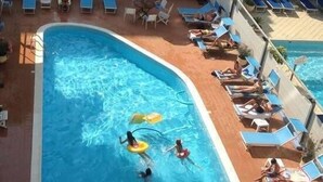 A swimming pool with lounge chairs and umbrellas, surrounded by a tiled deck. - Hotel Arena (Cattolica)