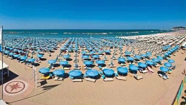 A beach with numerous blue umbrellas and sun loungers arranged in rows. - Hotel Arena (Cattolica)