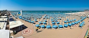 A beach with numerous blue umbrellas and sun loungers arranged in rows. - Hotel Arena (Cattolica)