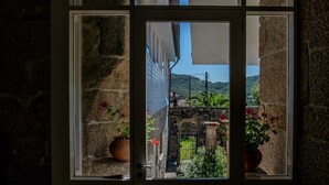 A stone wall with a window revealing a garden with potted plants and a view of a hillside. - Casa Rural O'Pozo (Cerdedo-Cotobade)