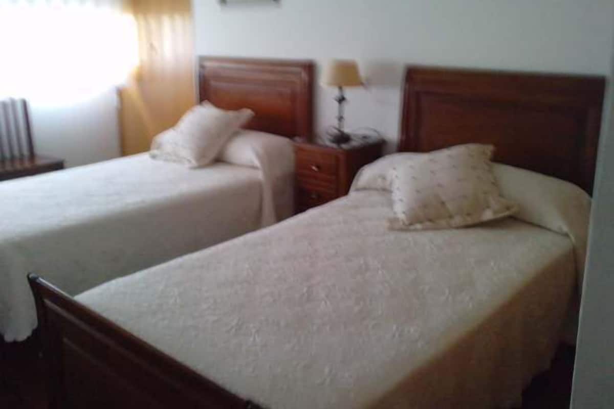A hotel room with two single beds, each with a wooden headboard, a bedside table with a lamp, and a framed picture on the wall.