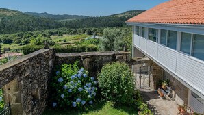 A stone wall with a garden featuring hydrangeas and a view of a valley with vineyards. - Casa Rural O'Pozo (Cerdedo-Cotobade)