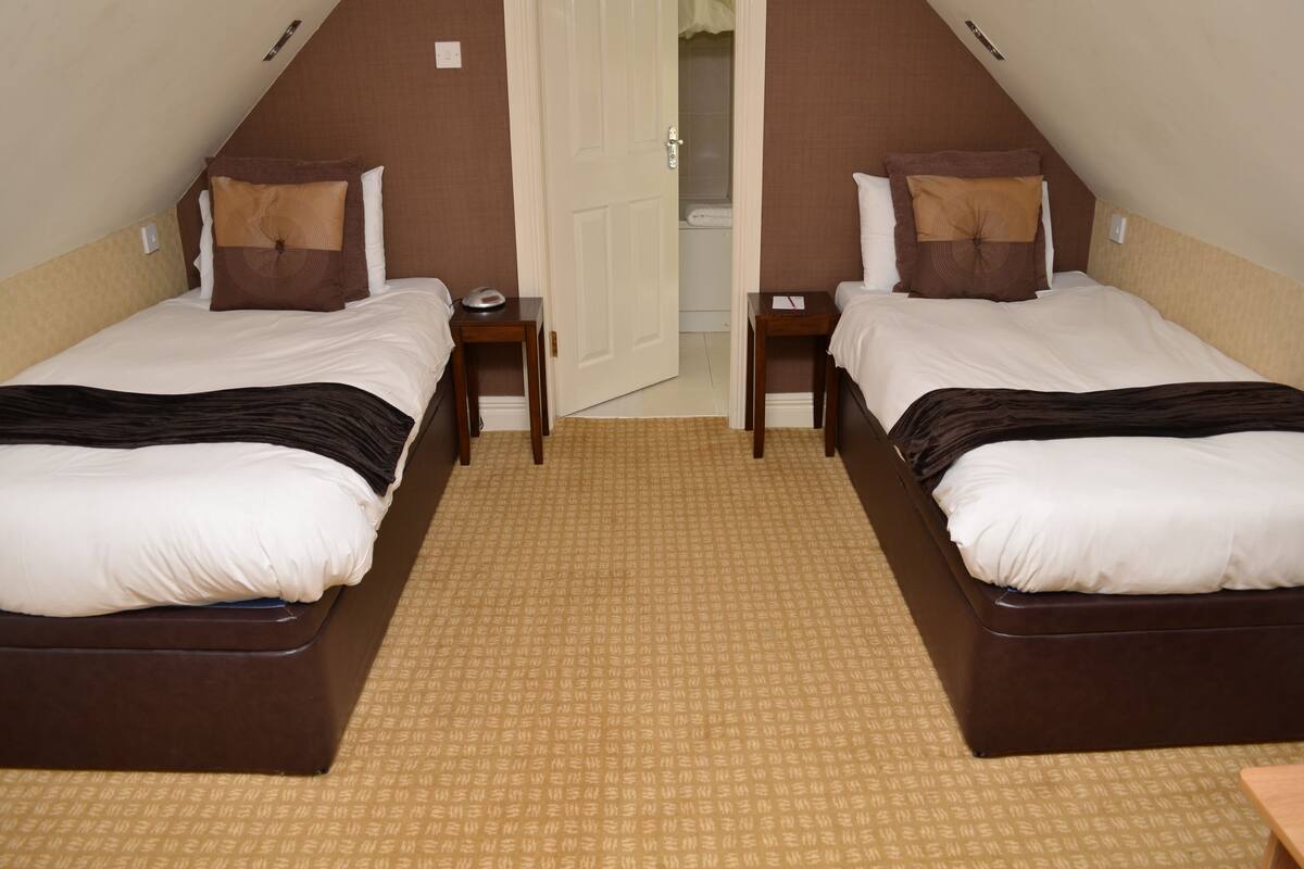 Une chambre d’hôtel avec deux lits, une petite table et une porte donnant sur une salle de bain.