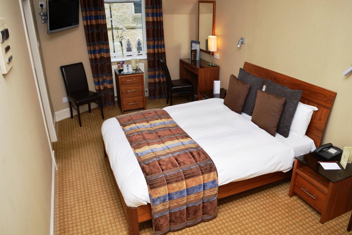 Une chambre d’hôtel avec un grand lit, un bureau, une chaise, une télévision et une fenêtre avec des rideaux.