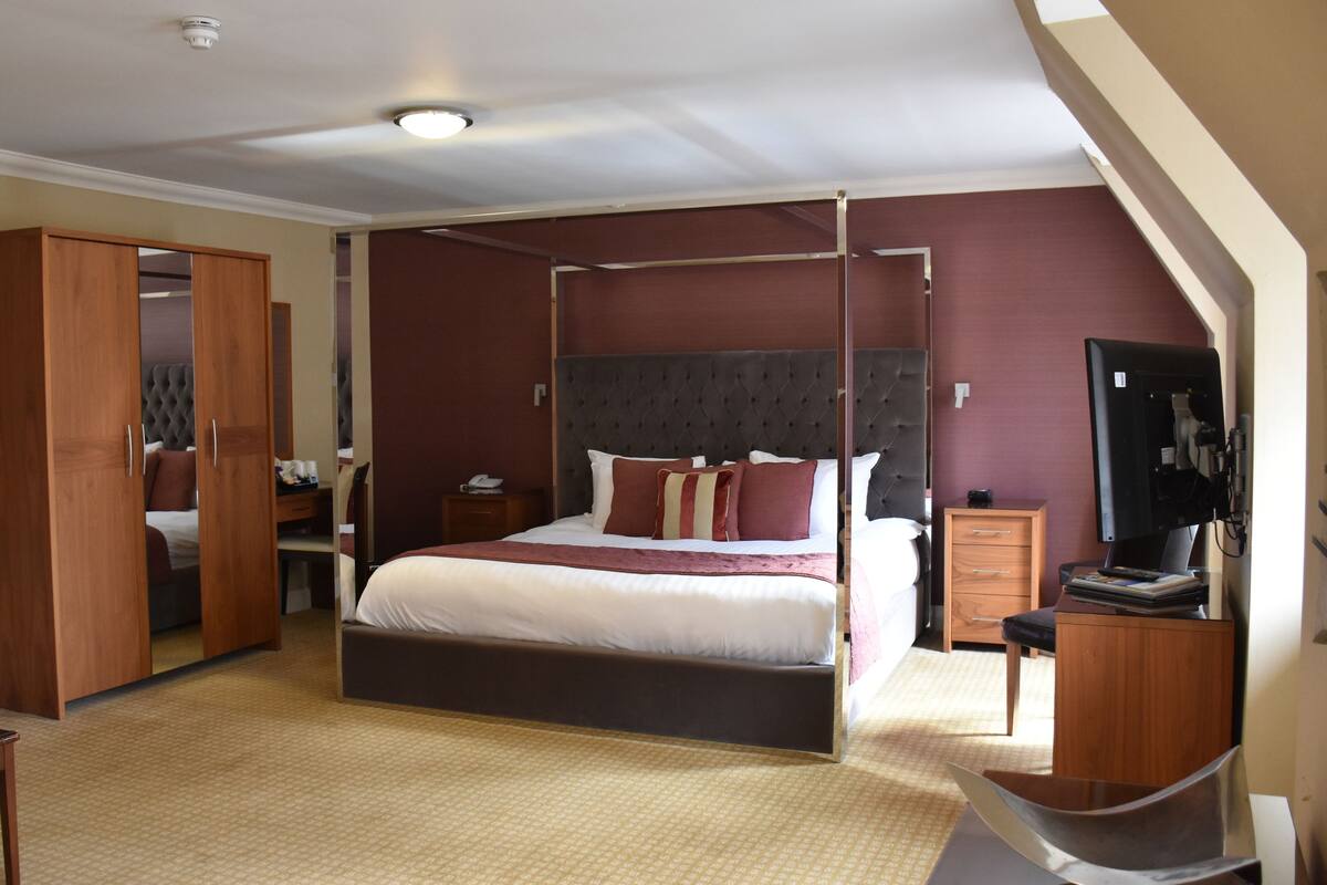 Une chambre à coucher avec un lit à baldaquin, une armoire en bois, des tables de chevet et un téléviseur.
