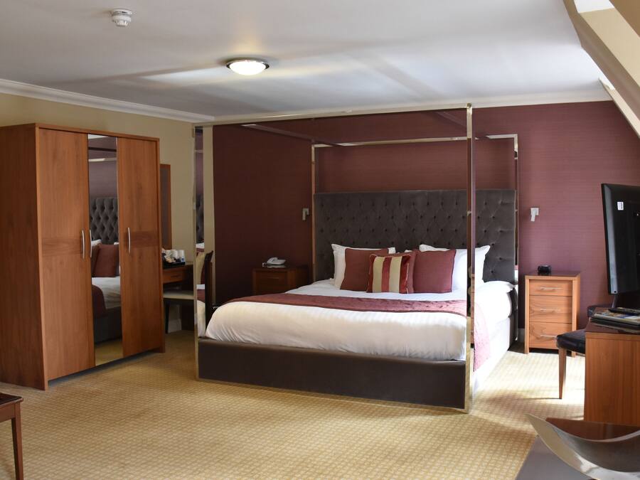 A bedroom with a four-poster bed, wooden wardrobe, bedside tables, and a television.