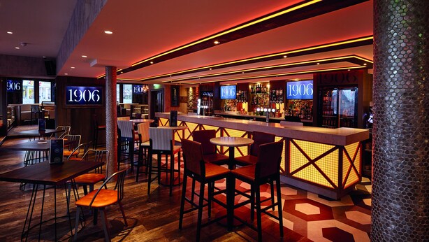 A bar area with a modern design, featuring a bar counter, seating, and illuminated signage. - The Royal Hotel (Cumnock)