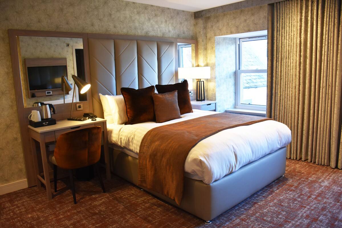 Une chambre d’hôtel avec un lit, un bureau et une chaise, une télévision et une fenêtre avec des rideaux.