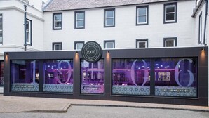 A building with a sign reading "Nineteen 06 1906" and large illuminated windows advertising "EAT - DRINK - ENJOY". - The Royal Hotel (Cumnock)
