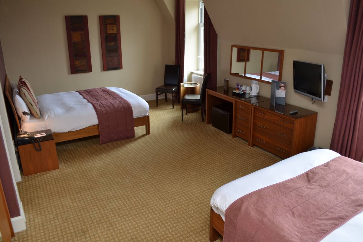 Une chambre d’hôtel avec deux lits, un bureau avec une chaise, une télévision et une fenêtre avec des rideaux.