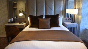 A hotel room with a large bed, a desk with a lamp, a chair, and a bedside table with a lamp. - The Royal Hotel (Cumnock)