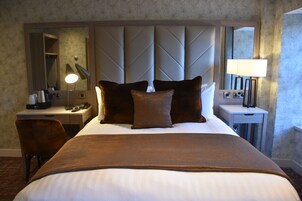 Quarto de hotel com uma cama grande, uma escrivaninha com luminária, uma cadeira e uma mesa de cabeceira com luminária.