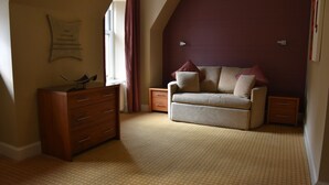 A bedroom with a sofa, wooden dresser, and a window with curtains. - The Royal Hotel (Cumnock)