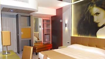 A modern hotel room with a bed, a desk, and a seating area.