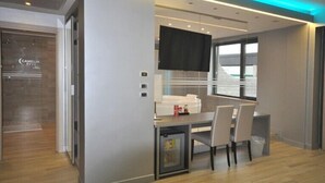 A modern hotel room with a dining area, a flat-screen TV, and a minibar. - Hotel Camelia (Cameri)