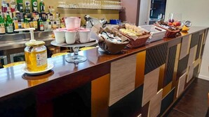 A bar area with a variety of beverages, including bottles and glasses, and a buffet setup with food items and baskets. - Hotel Camelia (Cameri)