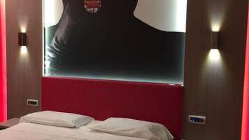 Una habitación de hotel con una cama grande, cabecera roja, una obra de arte colgada en la pared y una mesita de noche con un teléfono y un control remoto.