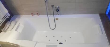 A modern bathroom with a large white bathtub, a handheld showerhead, and a towel rack.
