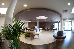 A spacious lobby with a reception desk, seating area, and large windows allowing natural light.