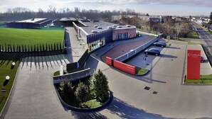 A modern building with a parking lot, a green field, and a red sign labeled "Camelia Hotel". - Hotel Camelia (Cameri)